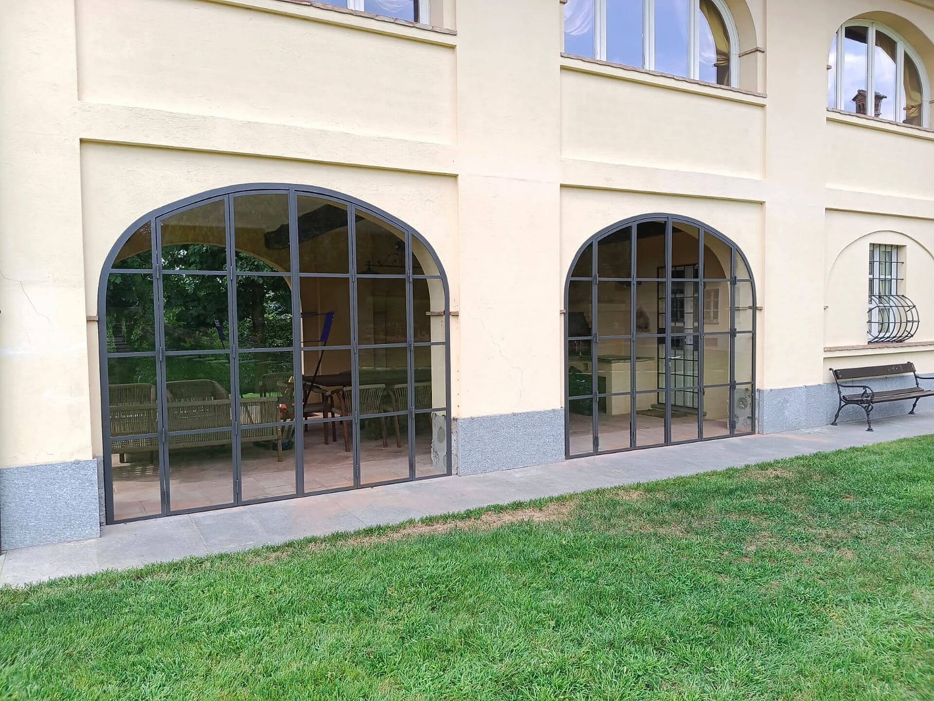 Due arcate del portico chiuse da vetrate a specchiatura fitta, viste dal prato lungo il fianco della villa