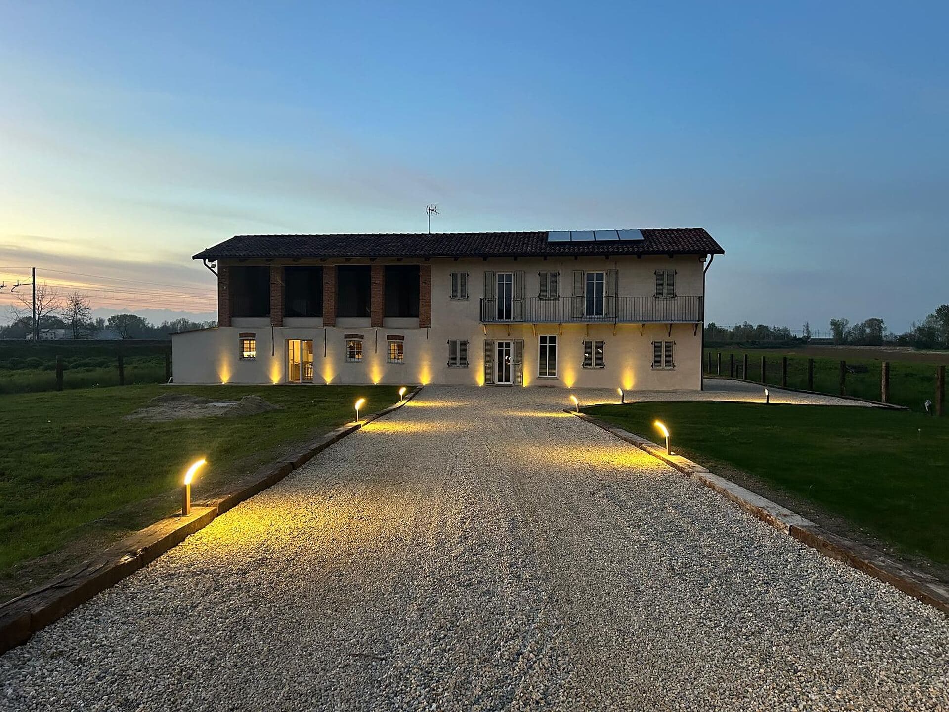 Il casale al crepuscolo, con le luci accese lungo il vialetto in ghiaia e il portico illuminato