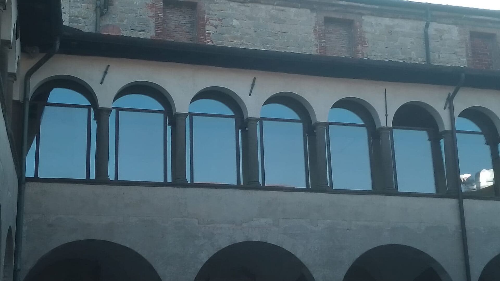 Il loggiato superiore del chiostro chiuso da vetrate continue, con le arcate in pietra che restano leggibili